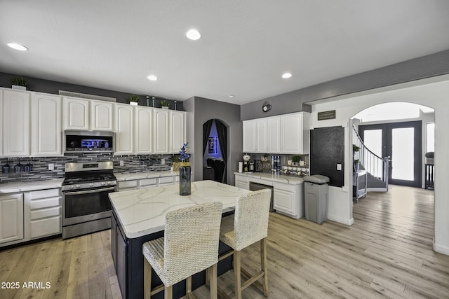 kitchen featuring arched walkways, tasteful backsplash, light stone counters, stainless steel appliances, and white cabinetry