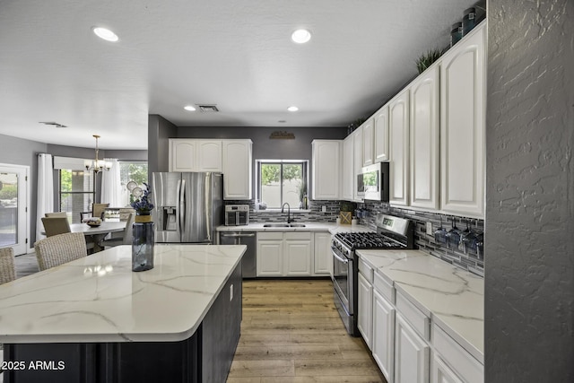 kitchen featuring appliances with stainless steel finishes, an inviting chandelier, a sink, backsplash, and visible vents