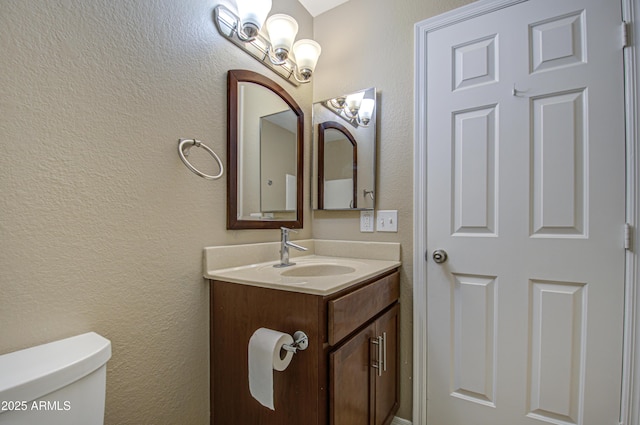 bathroom featuring toilet, a textured wall, and vanity