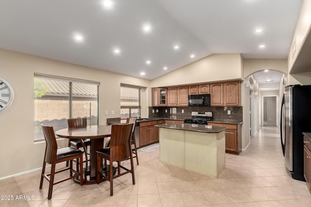 kitchen featuring dark stone countertops, stainless steel appliances, tasteful backsplash, a kitchen island, and vaulted ceiling