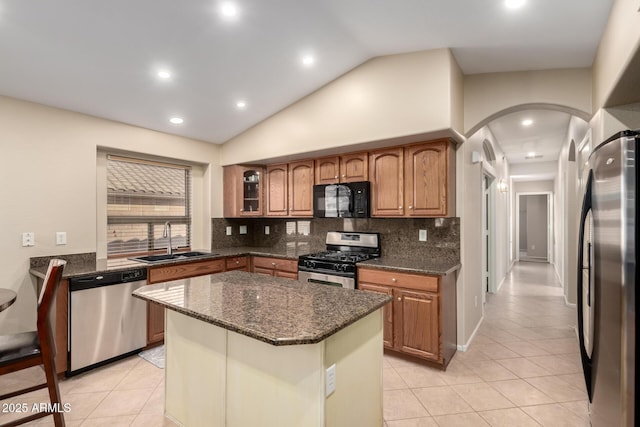 kitchen with a kitchen island, appliances with stainless steel finishes, lofted ceiling, sink, and dark stone countertops