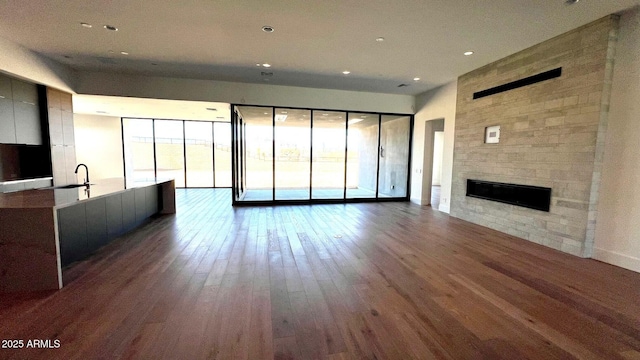 unfurnished living room featuring baseboards, a tiled fireplace, wood finished floors, a sink, and recessed lighting