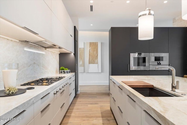 kitchen with sink, stainless steel appliances, hanging light fixtures, light hardwood / wood-style floors, and white cabinets