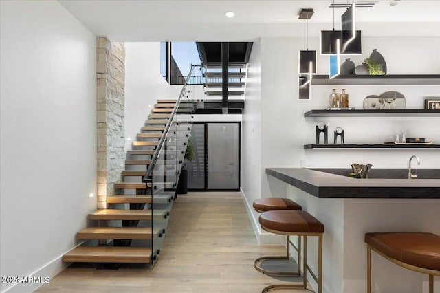 bar with light hardwood / wood-style floors, sink, and hanging light fixtures