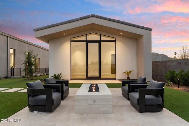 back house at dusk featuring a patio, a fire pit, and a lawn