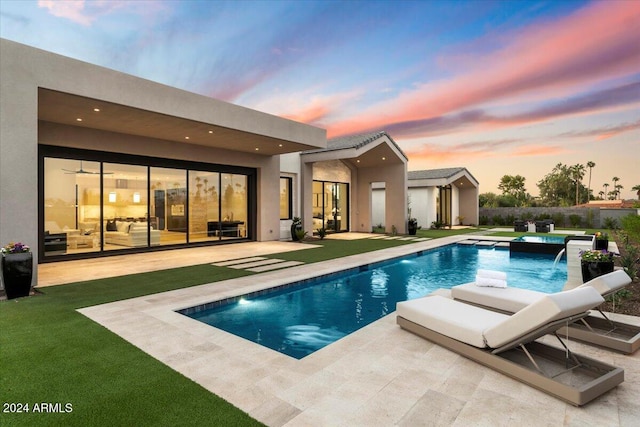 back house at dusk with pool water feature, a swimming pool with hot tub, and a patio