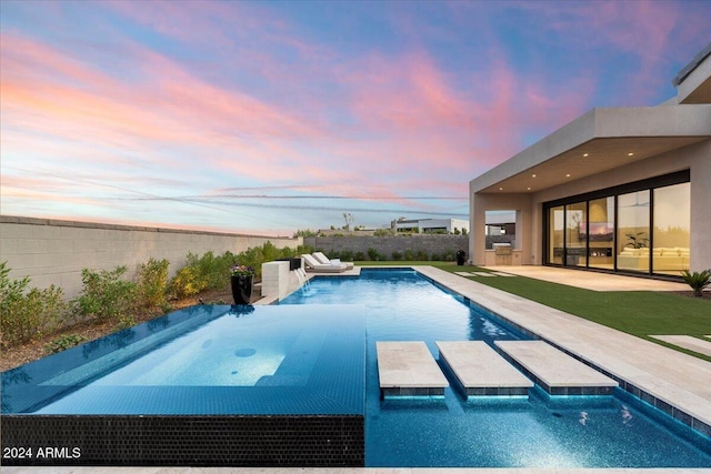 pool at dusk with a patio area, pool water feature, and a hot tub