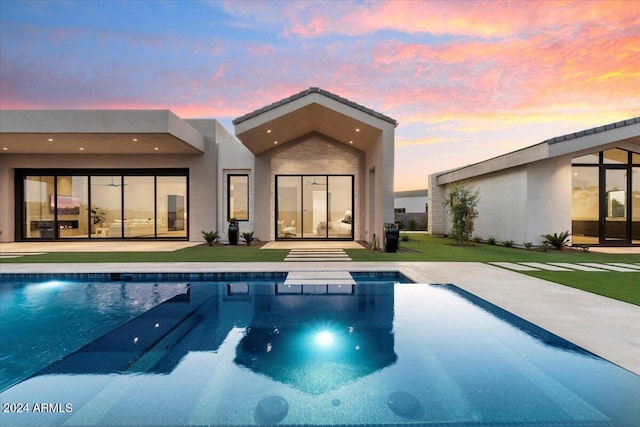 back house at dusk featuring a swimming pool with hot tub and a patio area