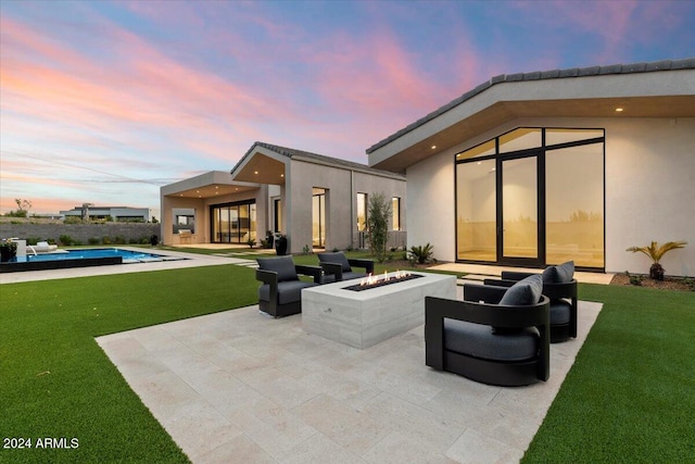 back house at dusk featuring a fire pit, a patio area, and a lawn