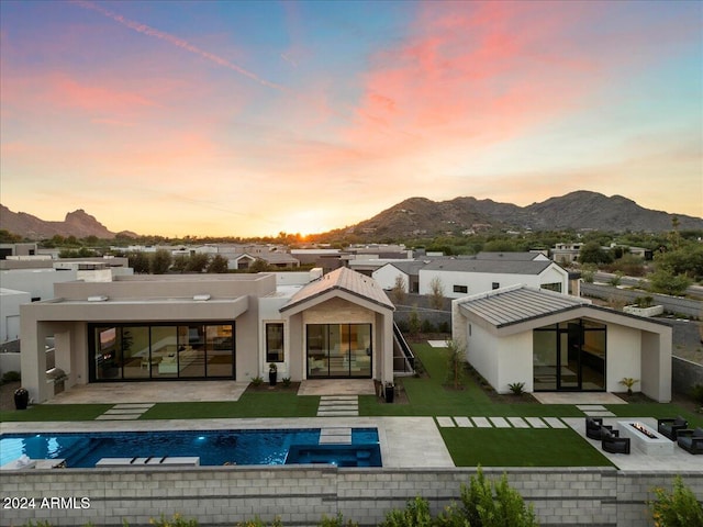 back house at dusk with a mountain view, a yard, and a patio