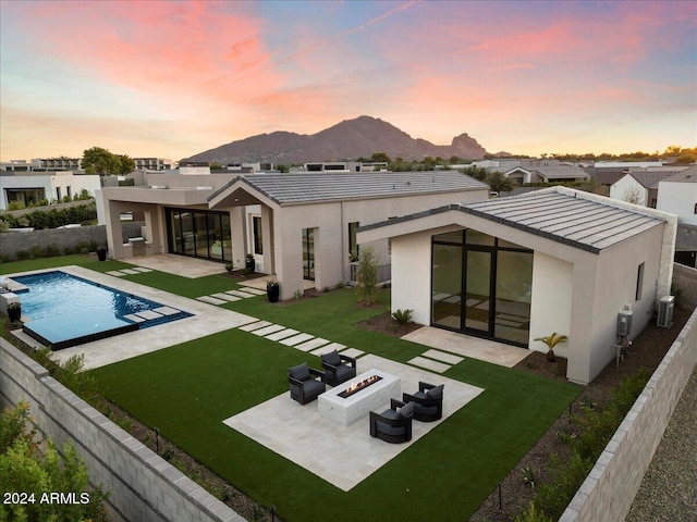 back house at dusk with a fire pit, a mountain view, a fenced in pool, a yard, and a patio