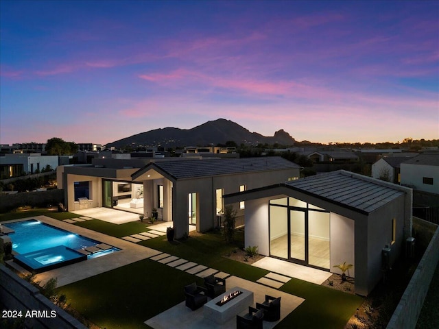 back house at dusk with a mountain view, a swimming pool with hot tub, a fire pit, and a patio area