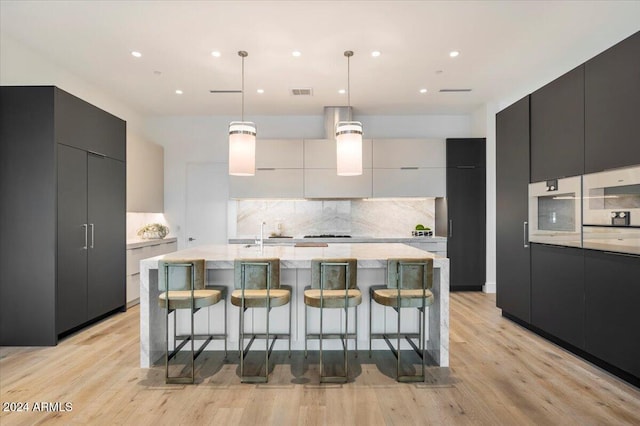 kitchen with a kitchen bar, light wood-type flooring, pendant lighting, a large island with sink, and white cabinetry