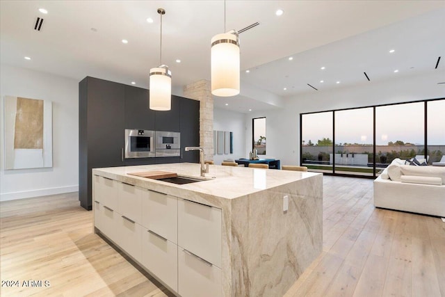 kitchen featuring pendant lighting, a large island with sink, oven, light hardwood / wood-style floors, and light stone counters