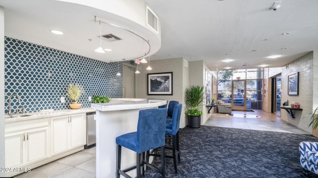 kitchen with an accent wall, a sink, white cabinetry, open floor plan, and a kitchen bar