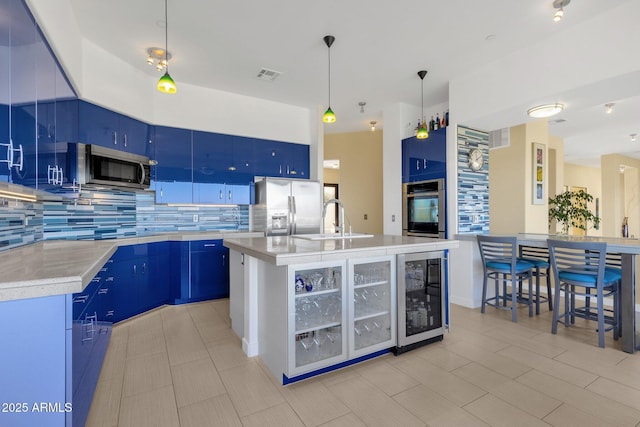 kitchen featuring stainless steel appliances, blue cabinets, beverage cooler, and an island with sink