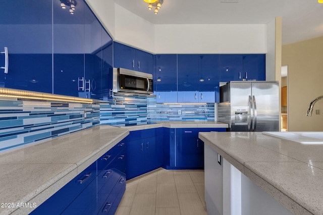 kitchen featuring blue cabinetry, decorative backsplash, stainless steel appliances, and sink