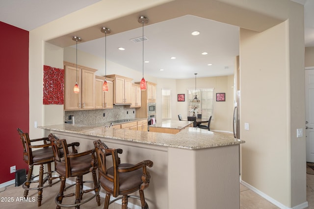 kitchen featuring light brown cabinetry, decorative backsplash, hanging light fixtures, kitchen peninsula, and light stone countertops