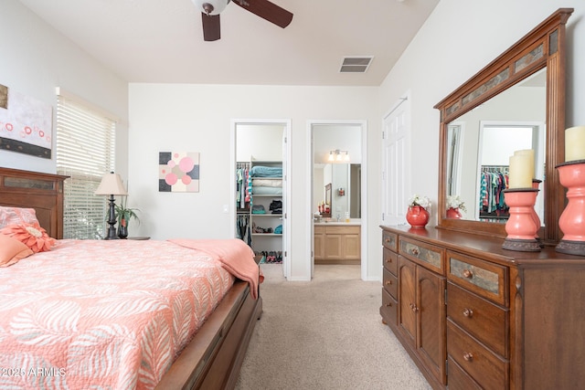 bedroom with a spacious closet, ceiling fan, light carpet, ensuite bath, and a closet