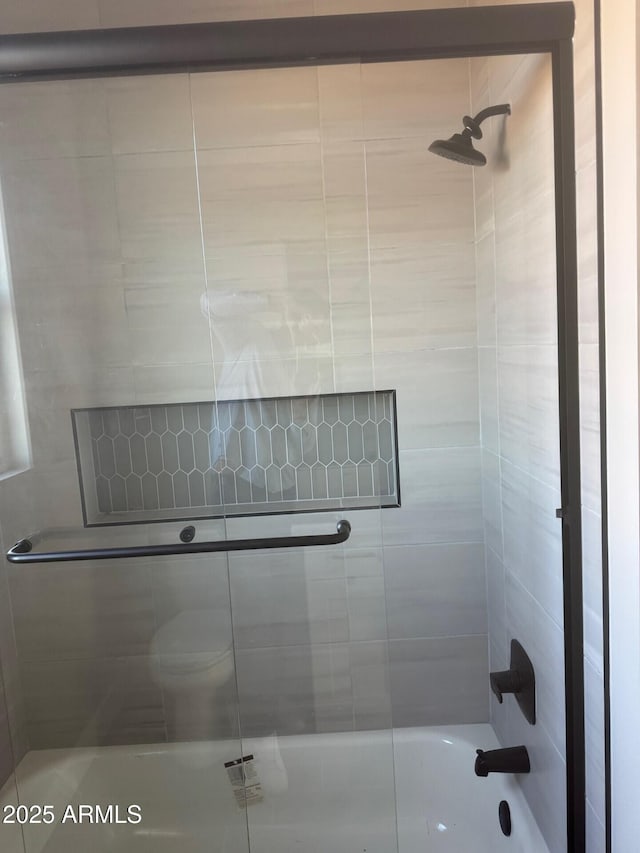 bathroom featuring combined bath / shower with glass door and toilet