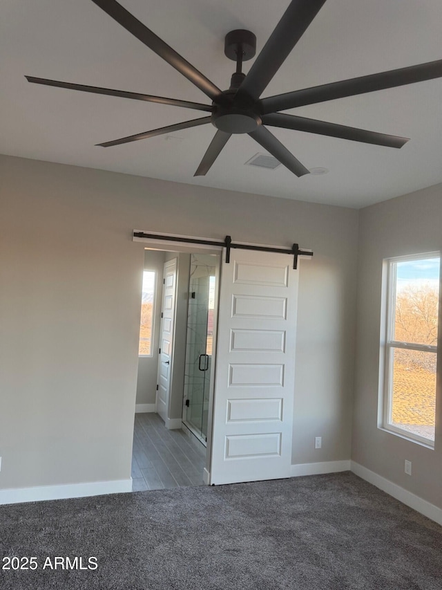 unfurnished bedroom featuring ceiling fan, a barn door, and carpet