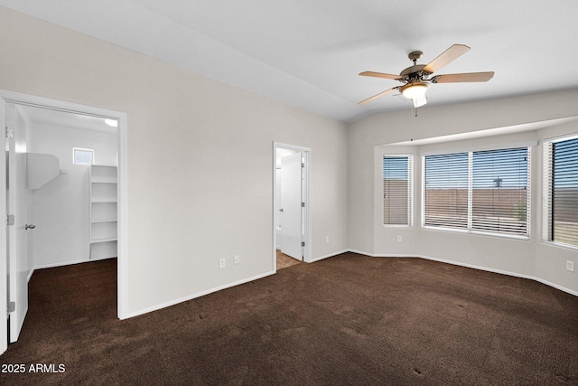 unfurnished bedroom featuring carpet floors, baseboards, vaulted ceiling, and a walk in closet