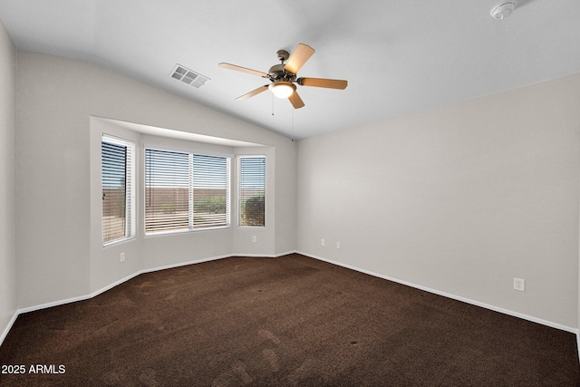 empty room with visible vents, baseboards, dark colored carpet, ceiling fan, and vaulted ceiling