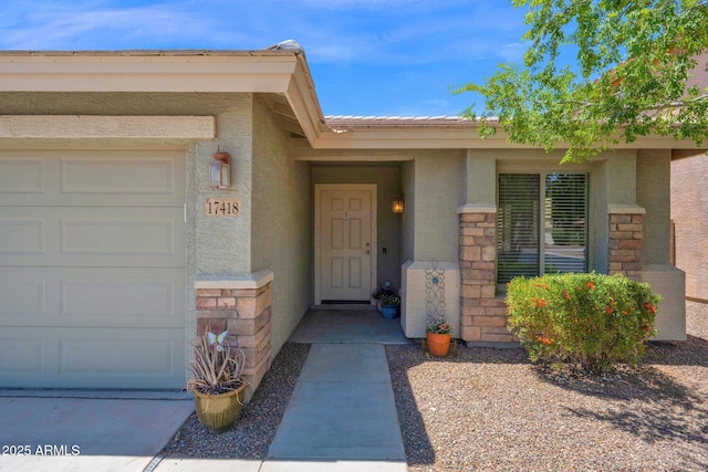 entrance to property with a garage, stone siding, and stucco siding