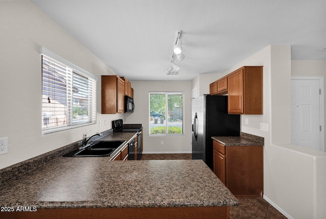 kitchen featuring dark countertops, brown cabinets, rail lighting, a sink, and black appliances