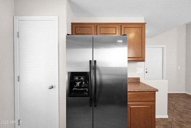 kitchen with dark tile patterned floors, baseboards, brown cabinetry, and stainless steel refrigerator with ice dispenser