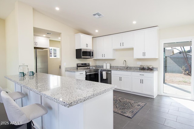 kitchen with sink, appliances with stainless steel finishes, white cabinetry, a kitchen bar, and kitchen peninsula