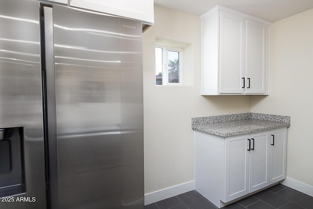 kitchen featuring white cabinetry, stainless steel fridge, light stone counters, and dark tile patterned flooring