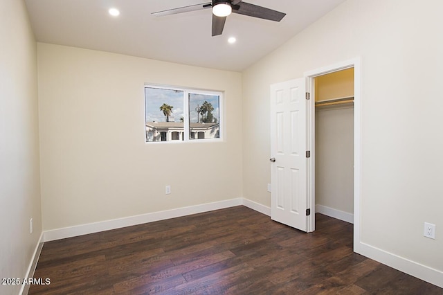 unfurnished bedroom with dark wood-type flooring, a walk in closet, vaulted ceiling, a closet, and ceiling fan