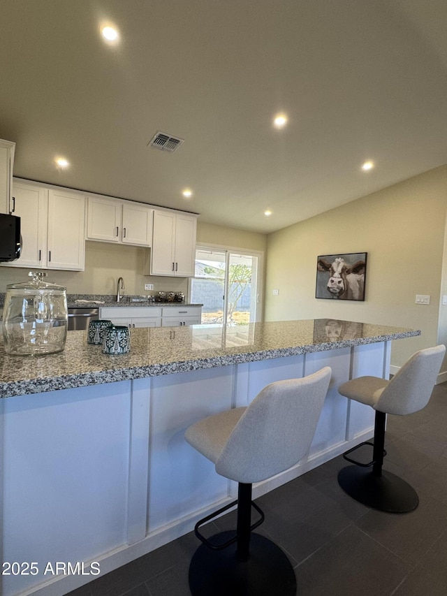 kitchen with sink, a breakfast bar area, white cabinets, and light stone counters