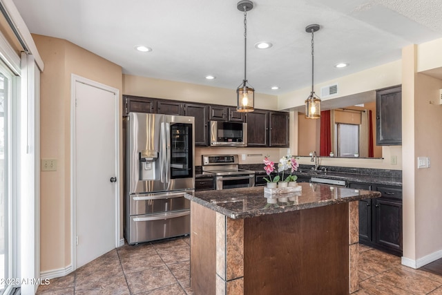 4114 E Muirwood Dr, Phoenix, AZ 85048 - kitchen with appliances with stainless steel finishes, a kitchen island, hanging light fixtures, dark brown cabinets, and dark stone countertops