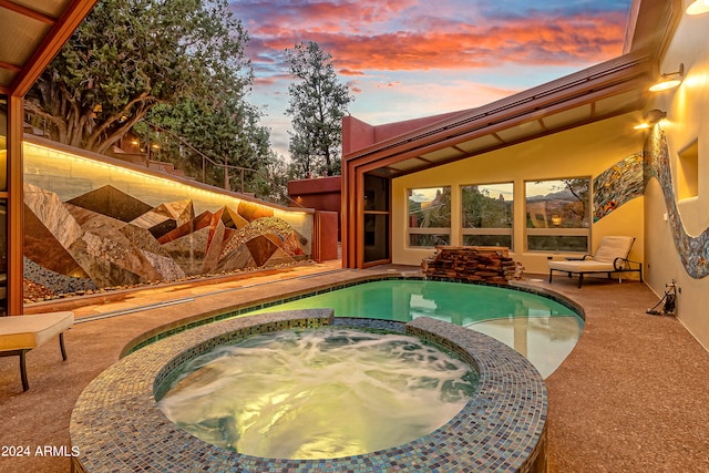 pool at dusk with an in ground hot tub and a patio