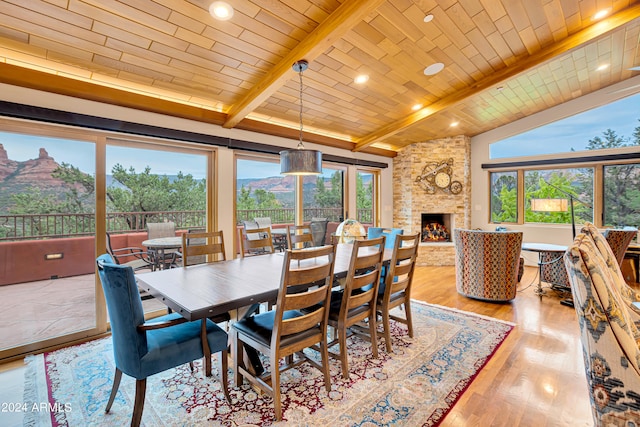 dining area with a stone fireplace, lofted ceiling with beams, wooden ceiling, light wood-type flooring, and a mountain view