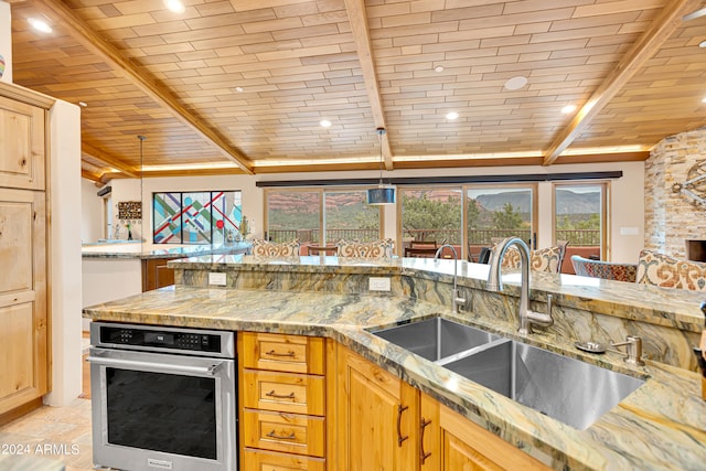 kitchen with decorative light fixtures, lofted ceiling with beams, sink, stainless steel oven, and light stone counters