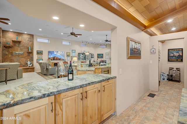 kitchen with light stone counters, ceiling fan, light brown cabinetry, and beamed ceiling