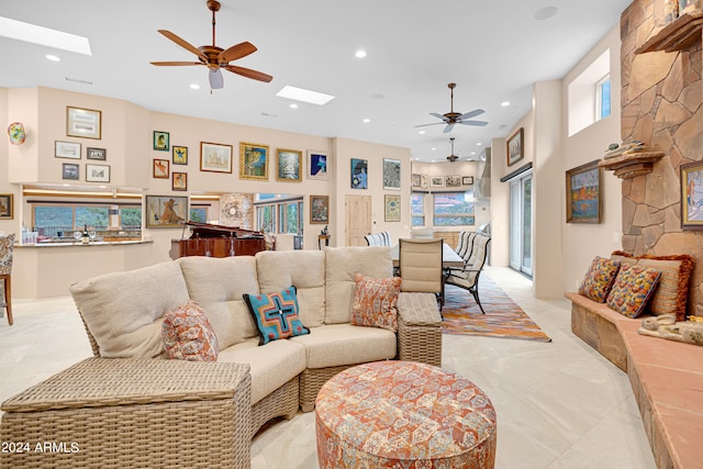 living room with ceiling fan, a skylight, and a towering ceiling