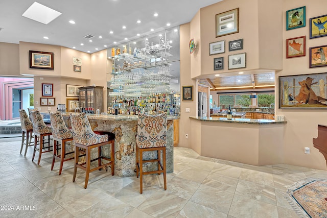 bar featuring a towering ceiling, high end refrigerator, and stone countertops