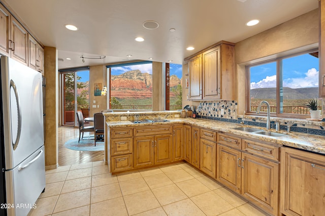 kitchen with sink, stainless steel fridge, light stone counters, kitchen peninsula, and a mountain view