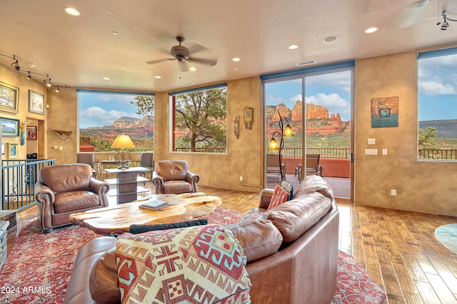 living room with a mountain view, rail lighting, ceiling fan, and light wood-type flooring