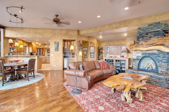 living room with a stone fireplace, ceiling fan, and light hardwood / wood-style flooring