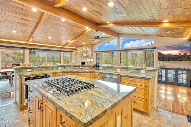 kitchen featuring a large island, vaulted ceiling with beams, light stone counters, and appliances with stainless steel finishes