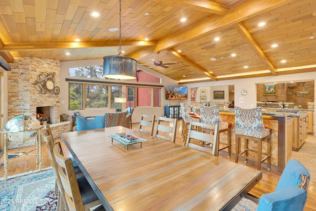 dining space with a stone fireplace, vaulted ceiling with beams, light hardwood / wood-style flooring, wooden ceiling, and ceiling fan