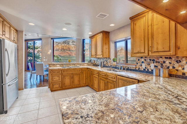 kitchen with sink, light tile patterned floors, stainless steel refrigerator, kitchen peninsula, and a healthy amount of sunlight