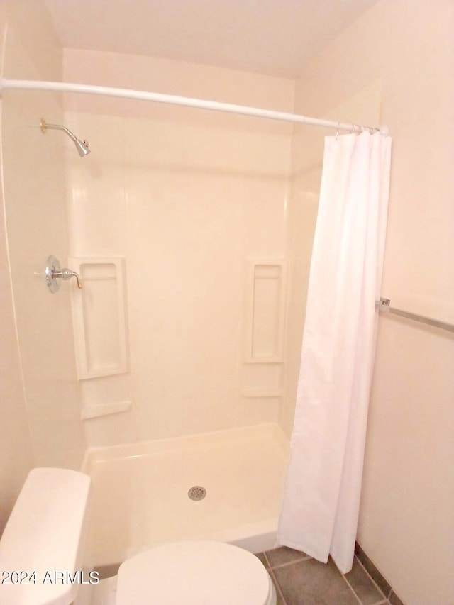 bathroom featuring toilet, curtained shower, and tile patterned flooring