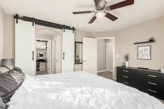 bedroom with ceiling fan, a barn door, a spacious closet, carpet floors, and a closet