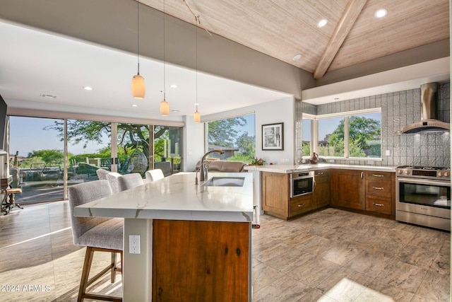 kitchen featuring stainless steel range with gas cooktop, a breakfast bar, decorative light fixtures, sink, and wall chimney exhaust hood